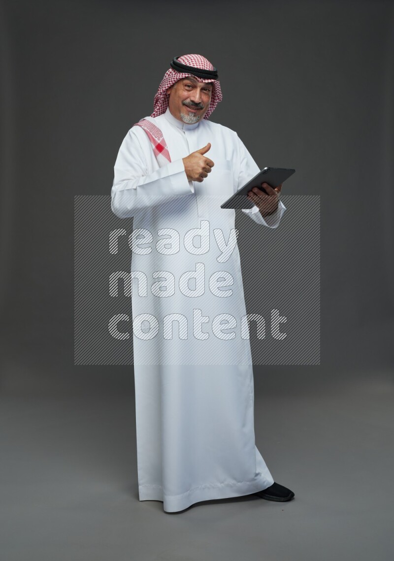 Saudi man with shomag Standing working on tablet on gray background
