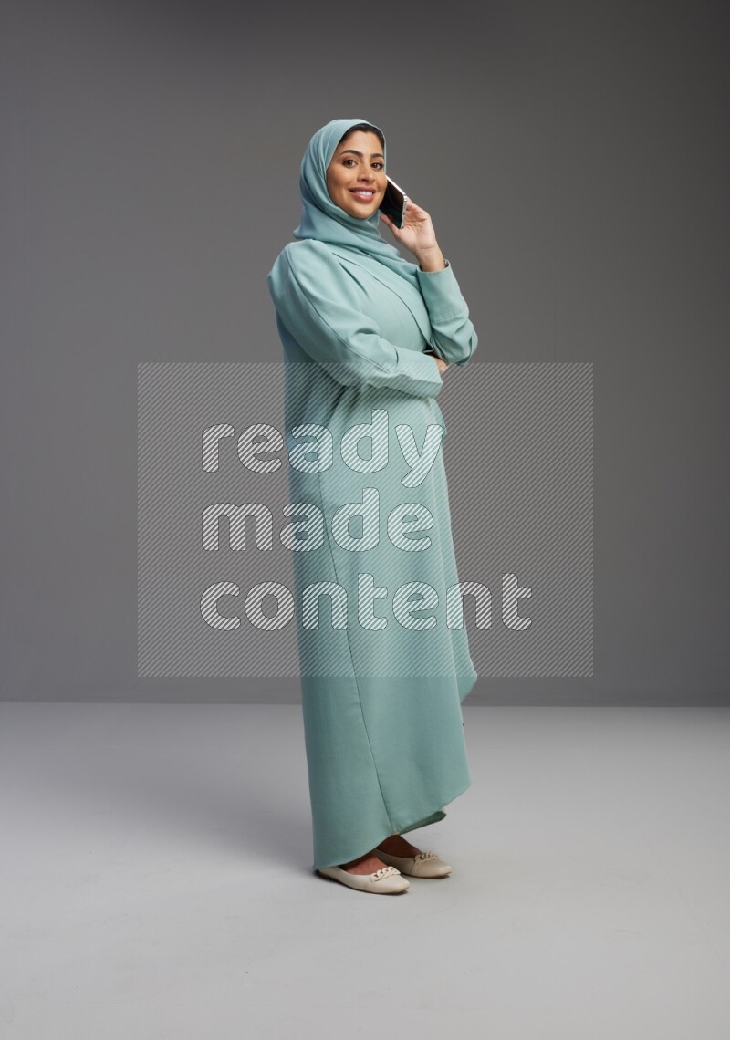 Saudi Woman wearing Abaya standing talking on phone on Gray background