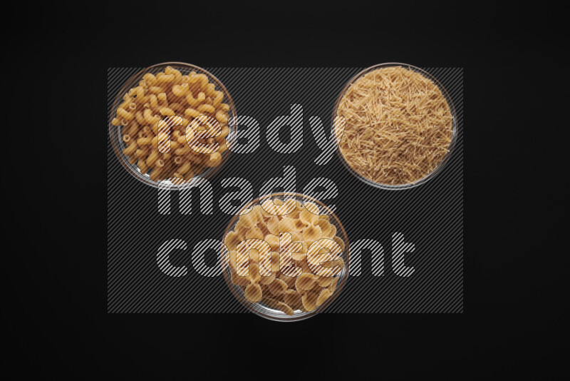 Different pasta types in glass bowls on black background