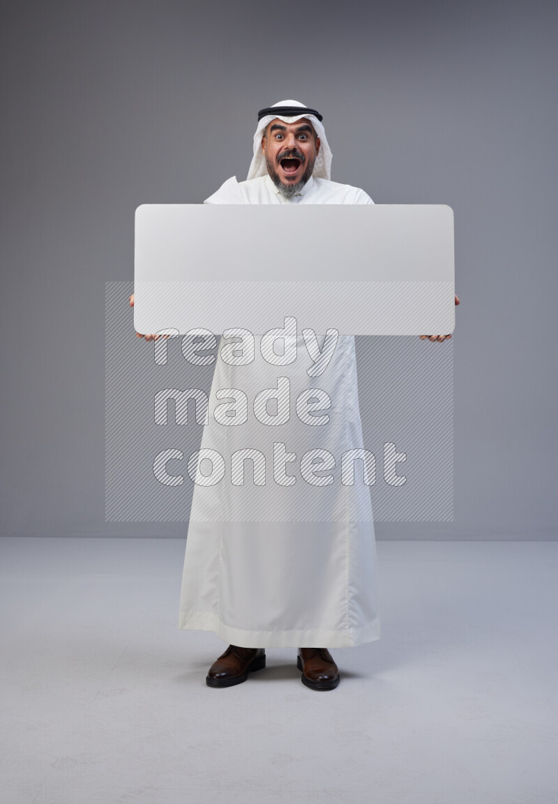 Saudi man Wearing Thob and white Shomag standing holding board on Gray background