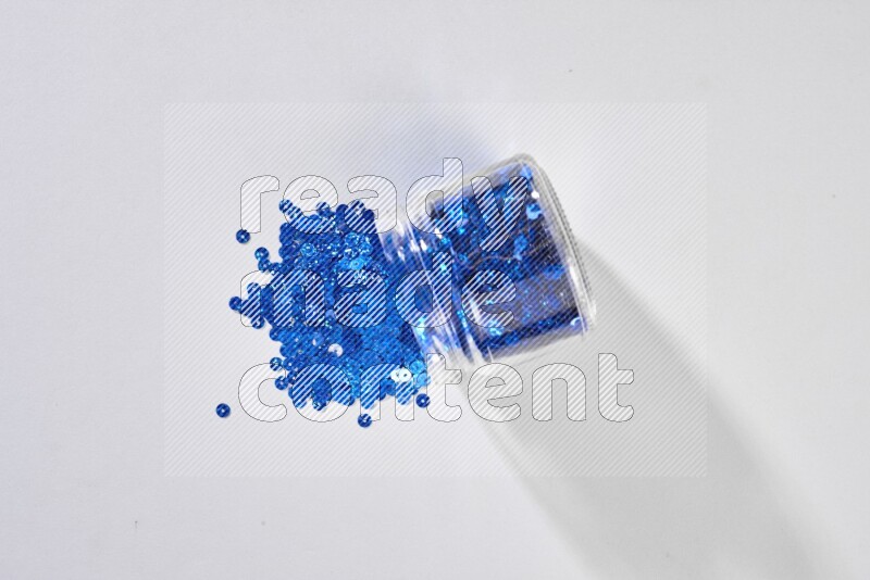 Colored flat sequins in a glass jar on grey background