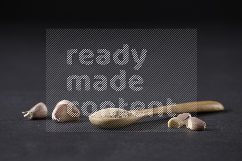 ملعقة خشبية مليئة ببودرة الثوم مع بعض فصوص الثوم على خلفية سوداء