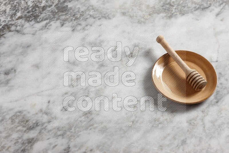 Beige pottery plate with wooden honey dipper in it on grey marble background