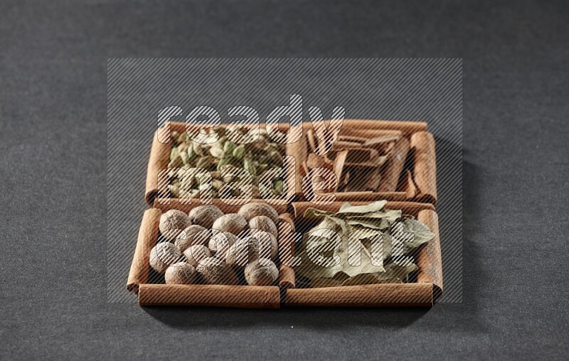 4 squares of cinnamon sticks full of cinnamon, cardamom, bay laurel leaves and nutmegs on black flooring