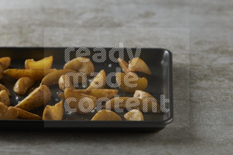 wedges potato in a black stainless steel rectangle tray on grey textured counter top