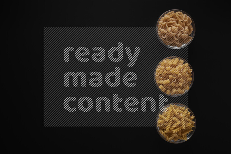 Different pasta types in 3 glass bowls on black background