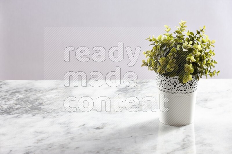 Green artificial plant in white decorative pot on grey marble background