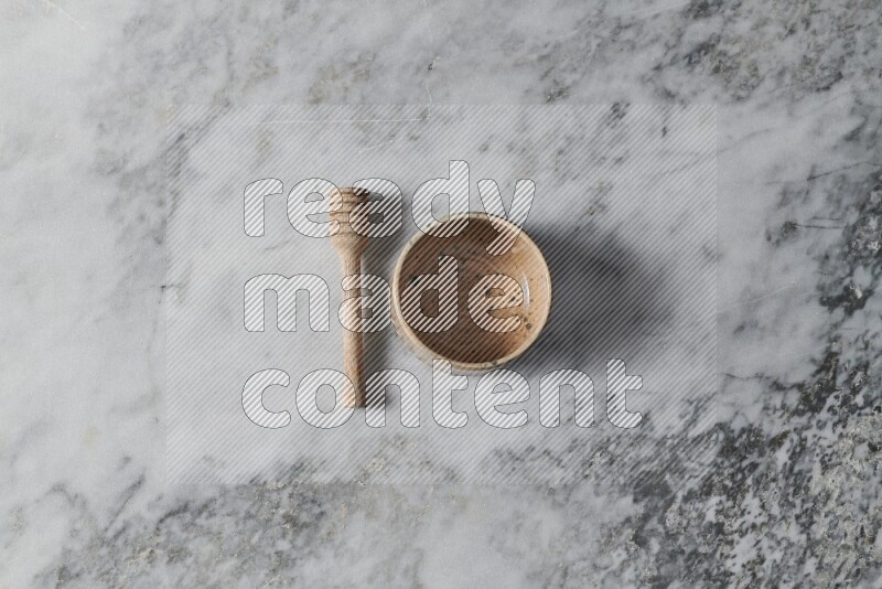 Multicolored pottery bowl with wooden honey dipper on the side on grey marble background