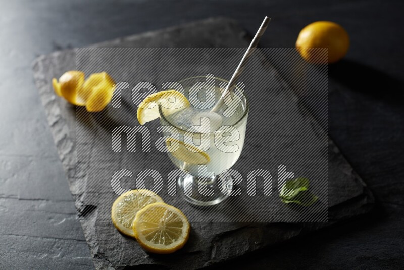 A glass of lemon juice with a straw on black background