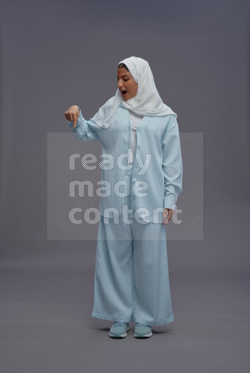 Saudi woman wearing hijab clothes standing interacting with the camera on gray background