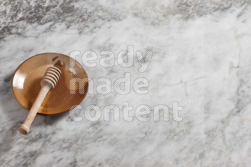 Multicolored pottery plate with wooden honey dipper in it on grey marble background