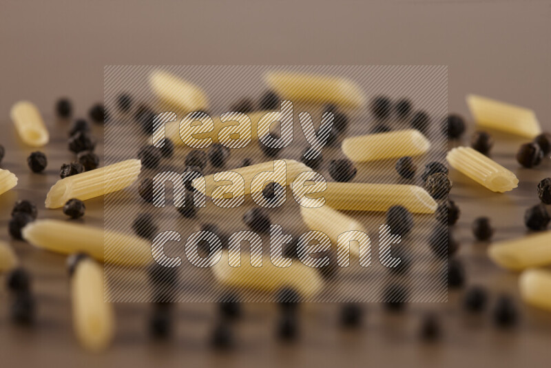 Raw pasta with different ingredients such as cherry tomatoes, garlic, onions, red chilis, black pepper, white pepper, bay laurel leaves, rosemary and cardamom on beige background