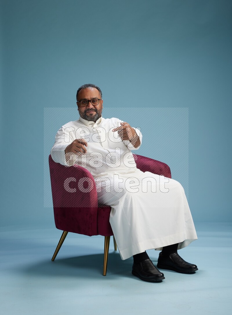 Saudi Man without shimag sitting on chair holding ATM card on blue background