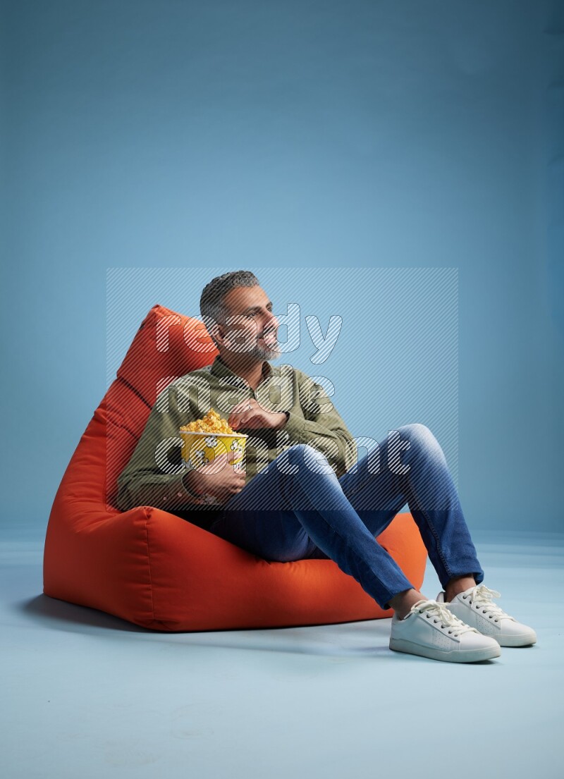 A man sitting on an orange beanbag and eating popcorn