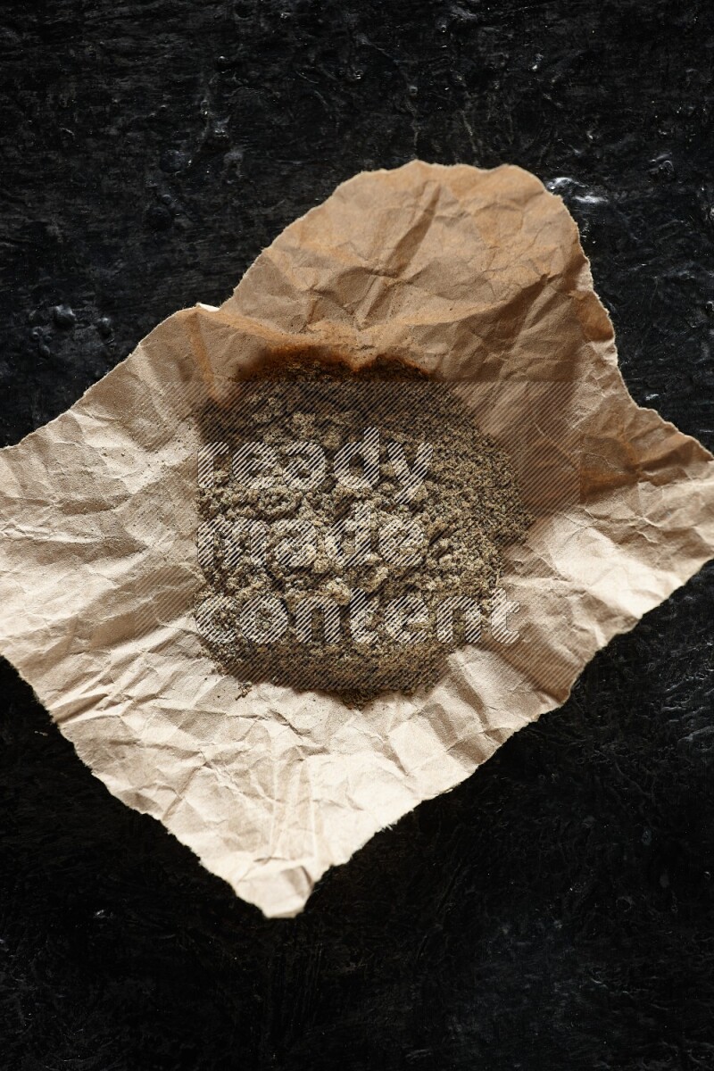 Cardamom powder in a crumpled piece of paper on textured black flooring
