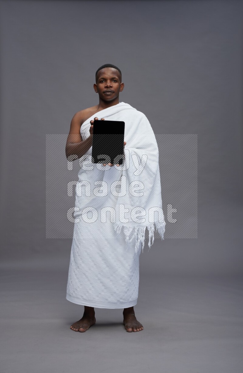 A man wearing Ehram Standing showing tablet to camera on gray background