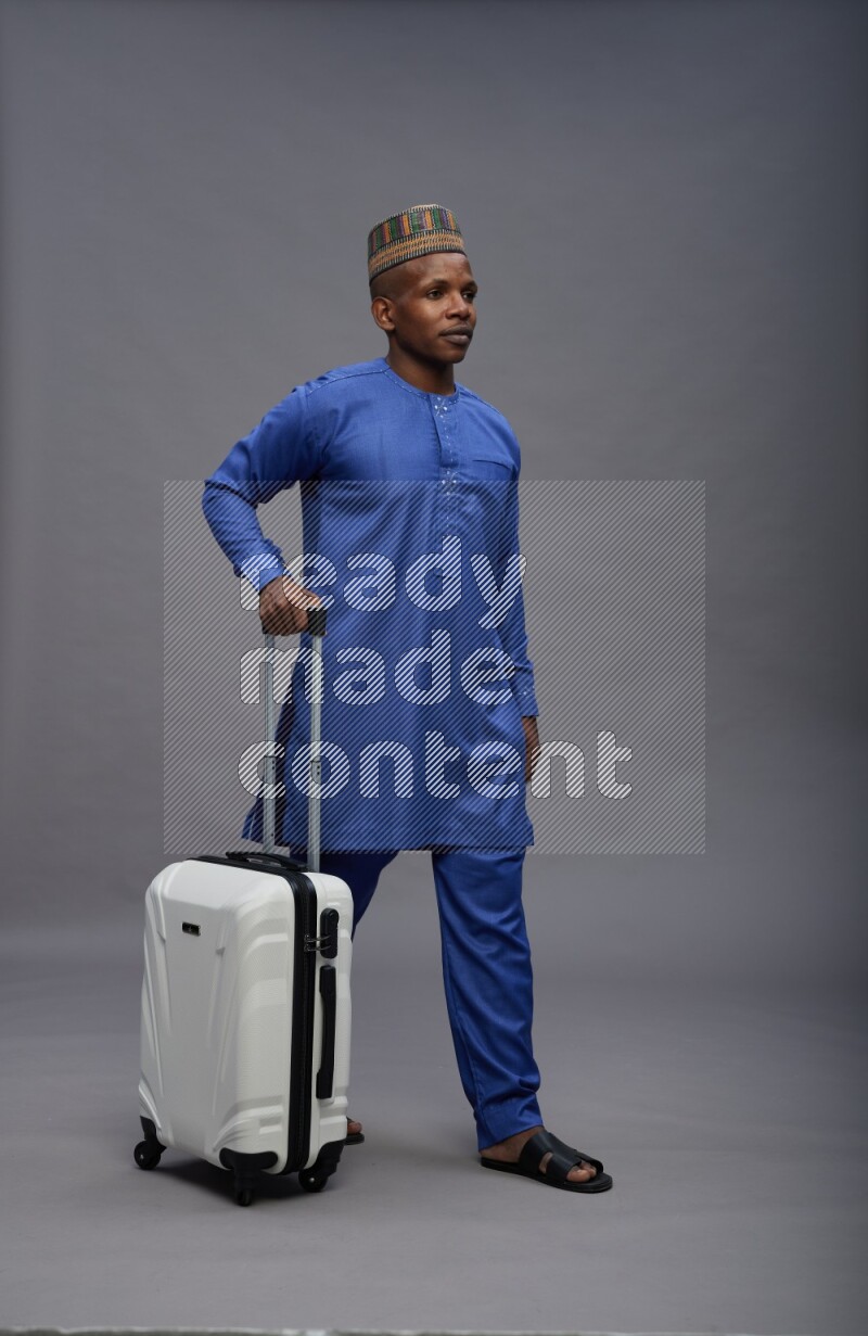 Man wearing Nigerian outfit standing holding bag on gray background