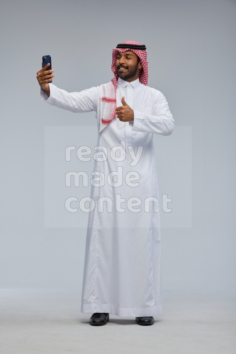 Saudi man Wearing Thob and shomag standing taking selfie on Gray background