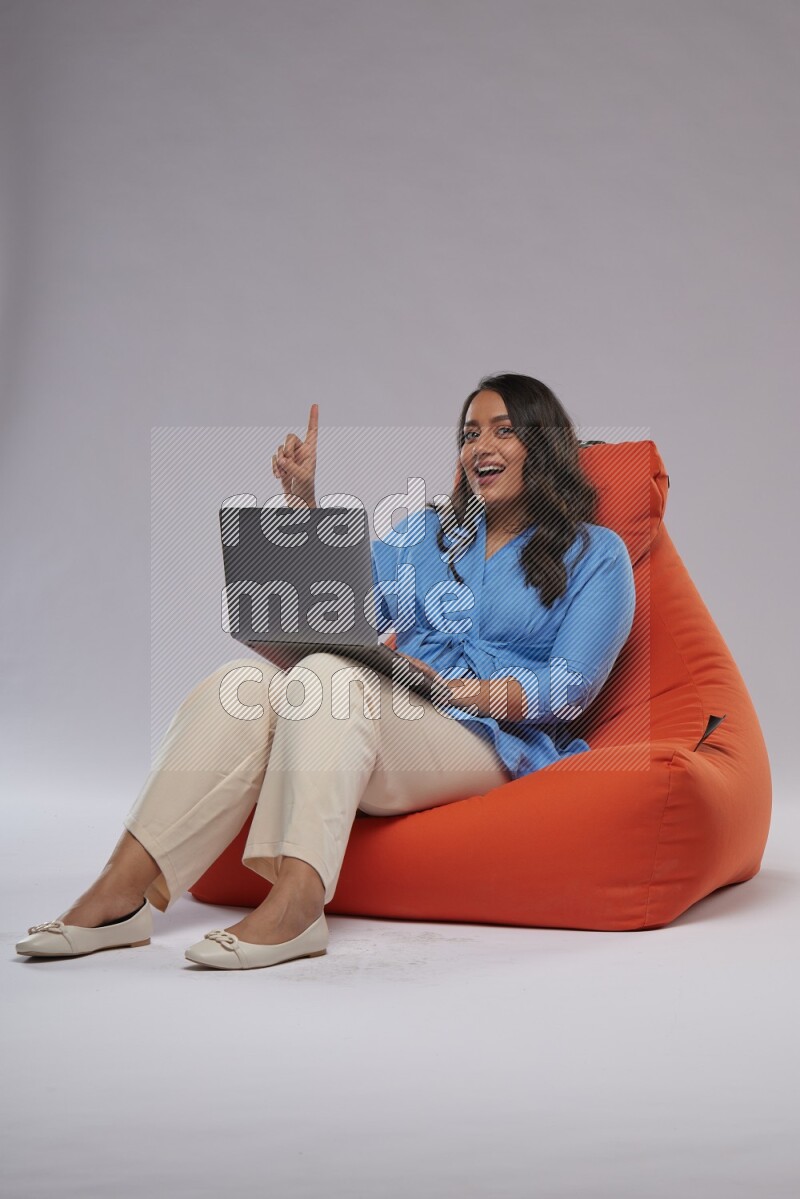 A woman sitting on an orange beanbag and working on laptop