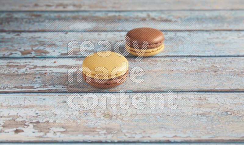 45º Shot of two Yellow and Brown Chai Latte macarons on light blue wooden background