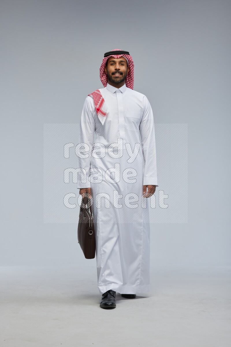 Saudi man Wearing Thob and shomag standing holding bag on Gray background