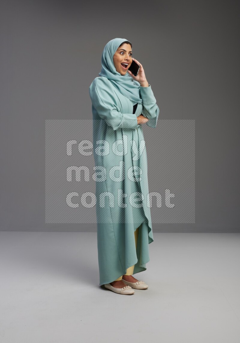 Saudi Woman wearing Abaya standing talking on phone on Gray background