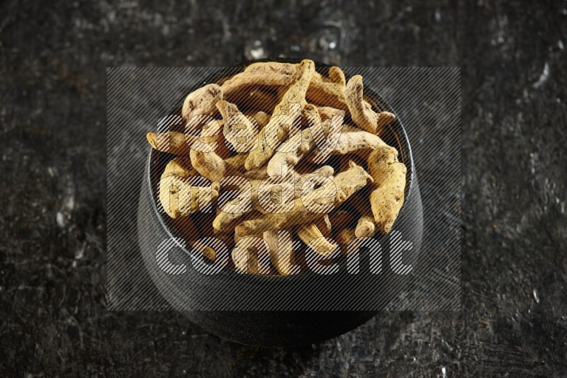 وعاء فخار أسود ممتلئ بأصابع كاملة من الكركم المجفف على خلفية سوداء