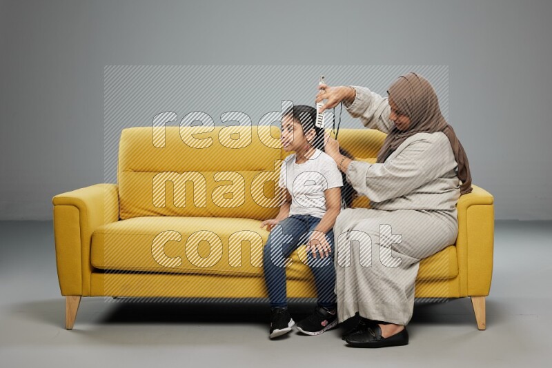 A mother sitting styling hair for her daughter on gray background