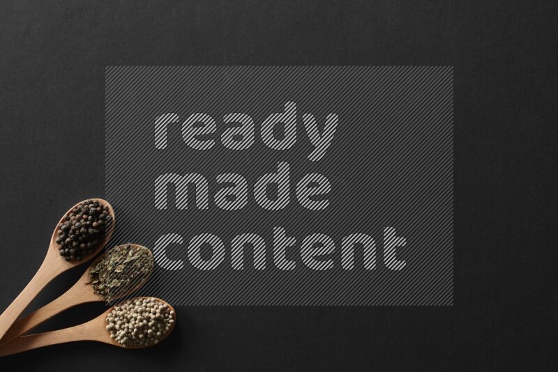 الفلفل الأبيض والقرنفل والهيل والملح والفلفل الأسود وريحان مجفف في معالق خشبية علي خلفية سوداء