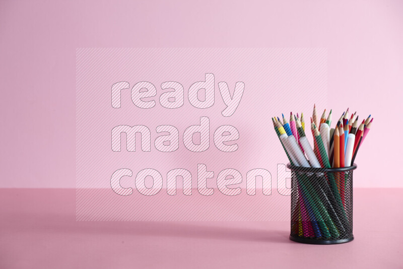Pens, pencils and other different school supplies in a metal pen holder on rose background