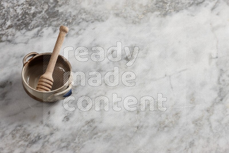 Multicolored pottery bowl with wooden honey dipper in it on grey marble background