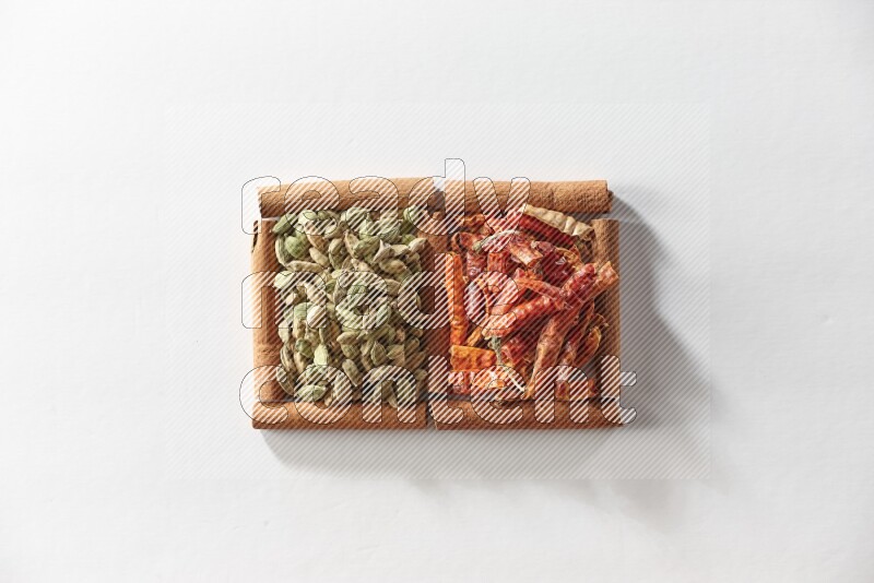 مربعان من أعواد القرفة ممتلئان بحبوب الهيل والفلفل الحار المجفف علي خلفية بيضاء