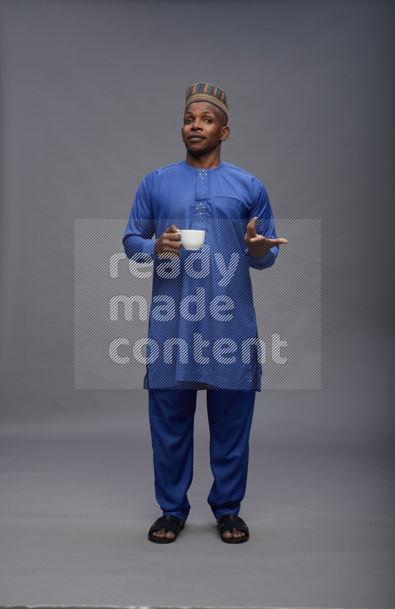 Man wearing Nigerian outfit standing holding mug on gray background