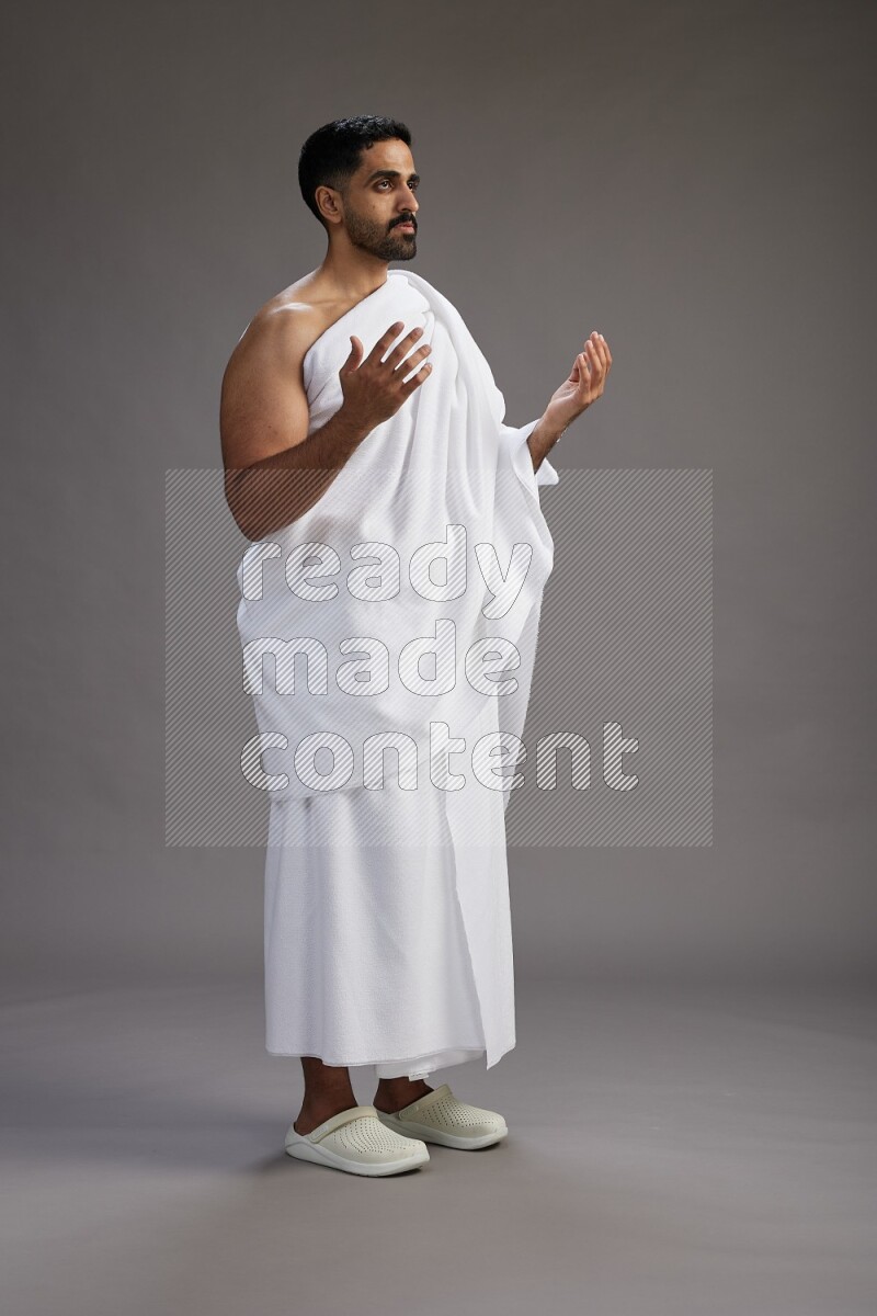 A man wearing Ehram Standing performing dua'a on gray background