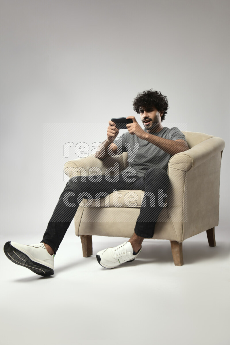 A man wearing casual sitting on a chair gaming on the phone on white background