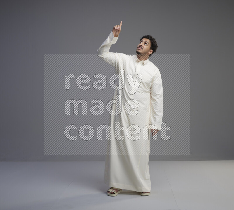 A Saudi man standing wearing thob interacting with the camera on gray background