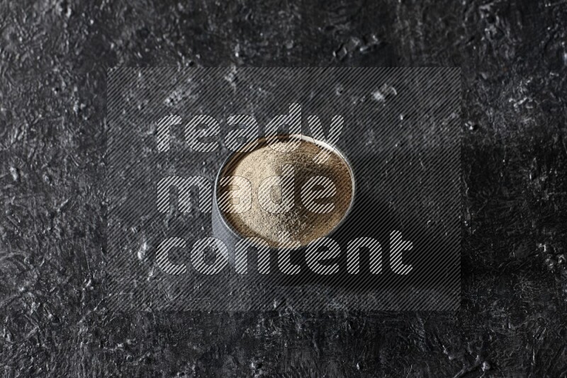 وعاء فخار أسود مملوء ببودرة الفلفل الأبيض على أرضية سوداء