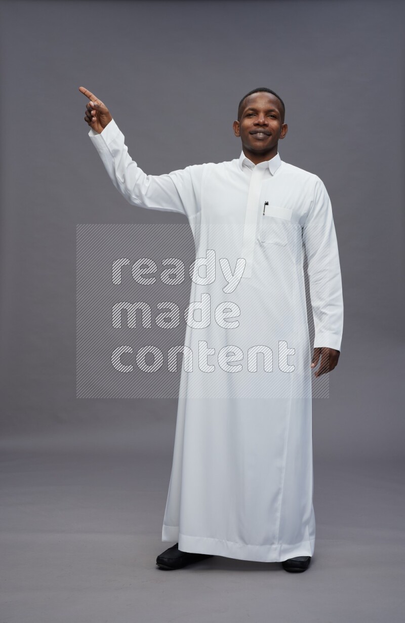 Saudi man wearing thob standing interacting with the camera on gray background