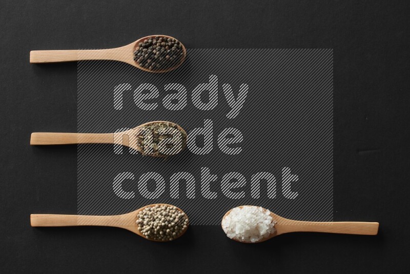 الفلفل الأبيض والقرنفل والهيل والملح والفلفل الأسود وريحان مجفف في معالق خشبية علي خلفية سوداء