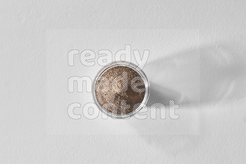 A glass bowl full of black pepper powder on white flooring