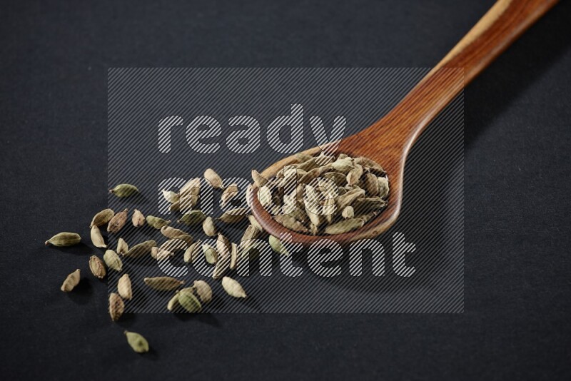 A wooden ladle full of cardamom on black flooring