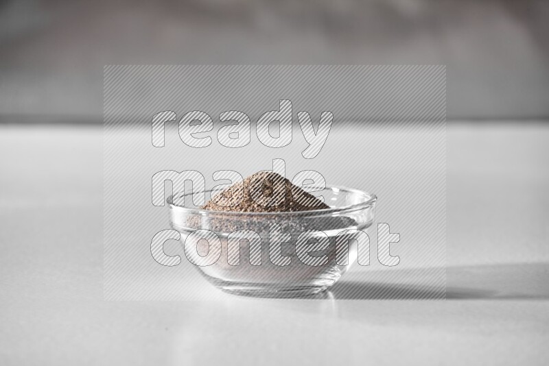 A glass bowl full of black pepper powder on white flooring