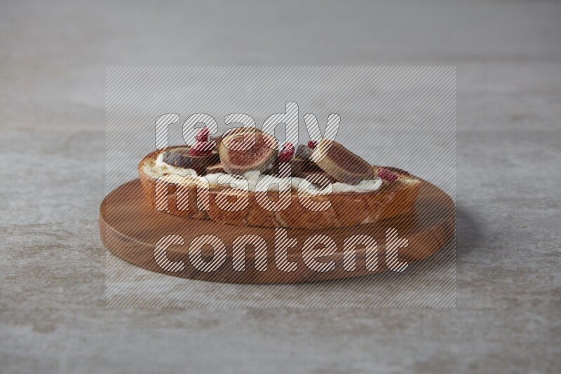 figs slices  with cream cheese on toasted sourdough slice on a wooden board on textured grey background