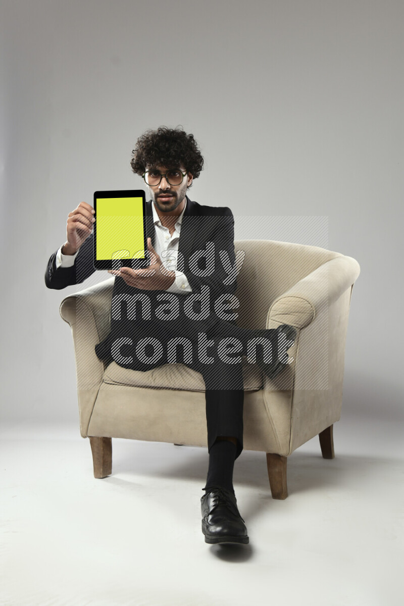 A man wearing formal sitting on a chair showing a tablet screen on white background