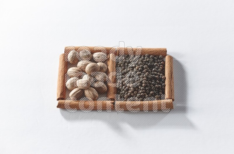 مربعان من أعواد القرفة ممتلئان بحبوب الفلفل الأسود وجوزة الطيب علي خلفية بيضاء