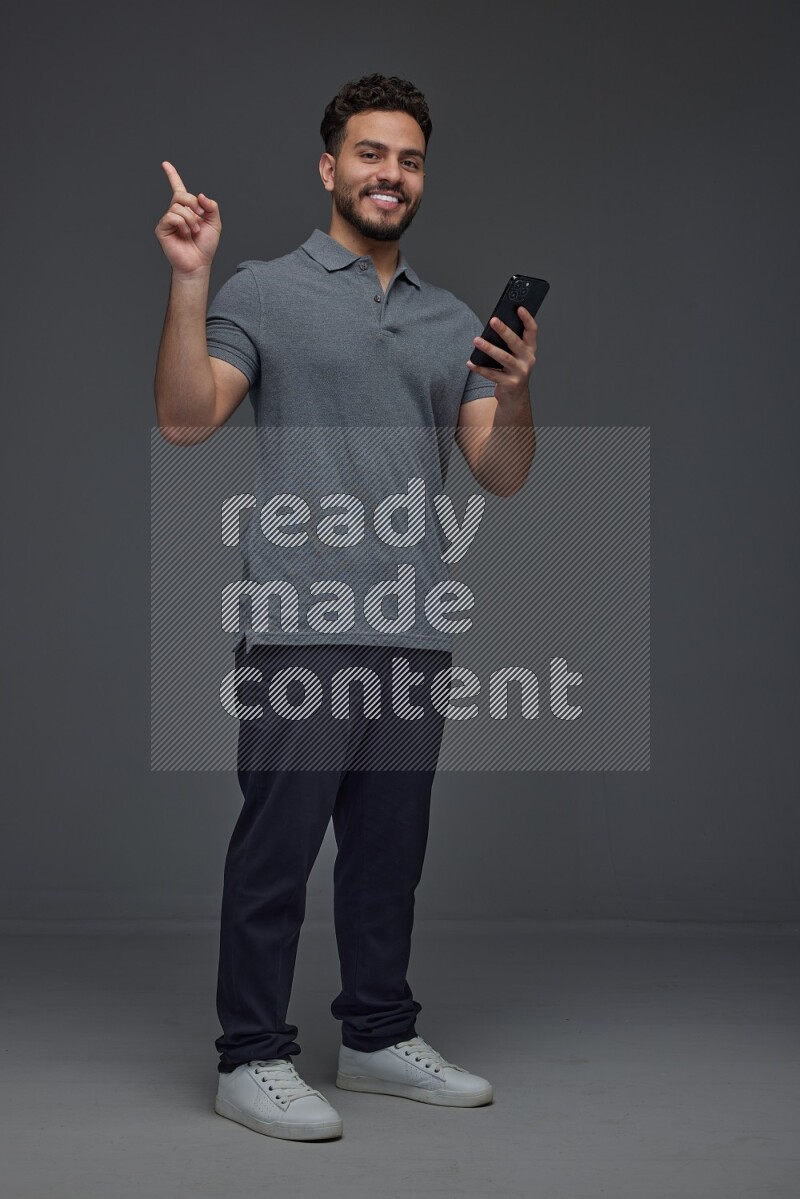 A man wearing casual standing and using his phone and making multi hand gestures eye level on a gray background