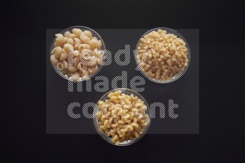 Different pasta types in glass bowls on black background