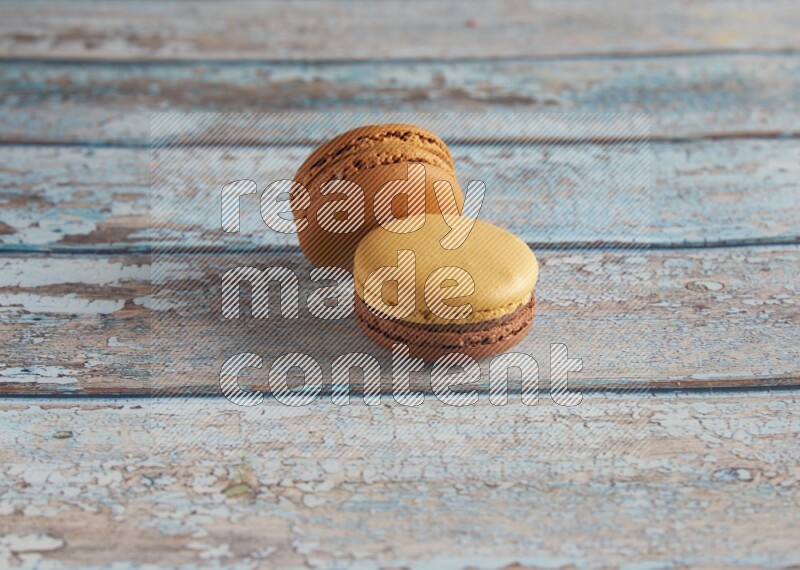 45º Shot of of two assorted Brown Irish Cream, and Yellow, and Brown Chai Latte macarons  on light blue background