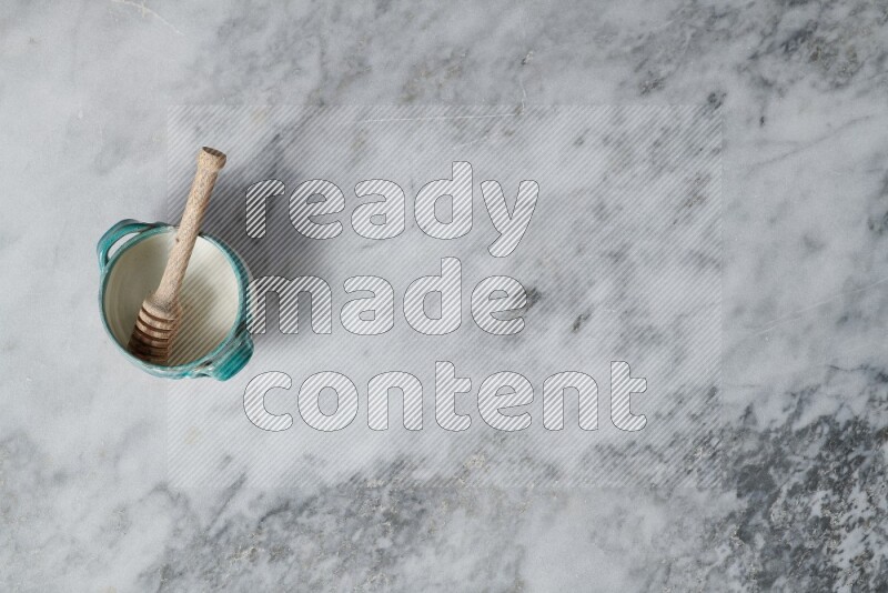 وعاء فخاري متعدد الألوان مع ملعقة عسل خشبية بداخله على خلفية من الرخام الرمادي