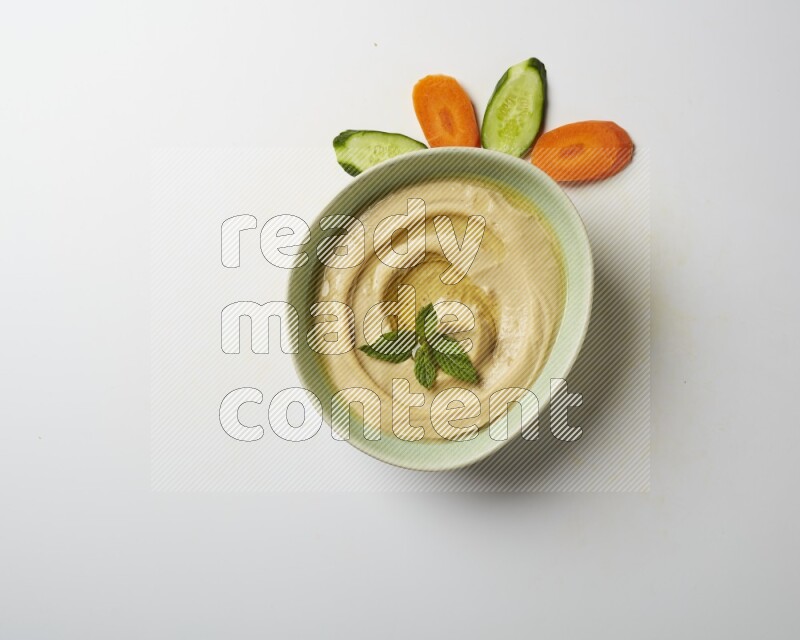 Hummus in a green plate garnished with mint on a white background